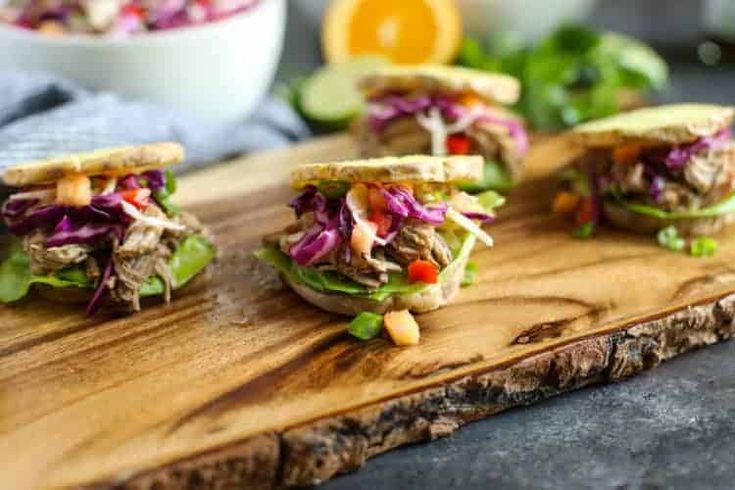 three sandwiches with lettuce, tomatoes and other vegetables on a wooden cutting board