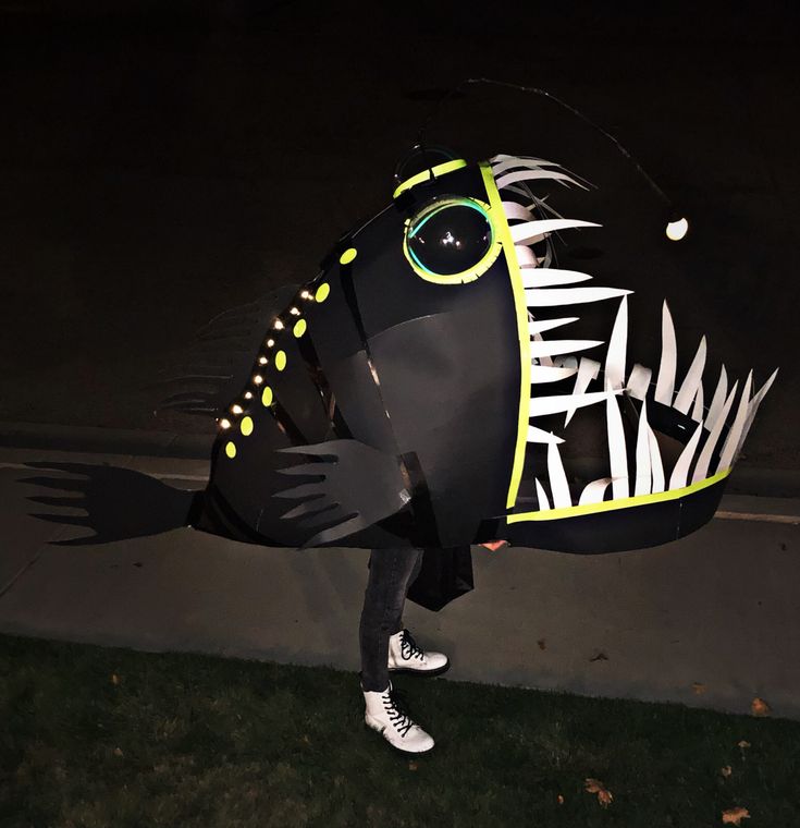 a person standing next to a black and white fish shaped kite on the grass at night