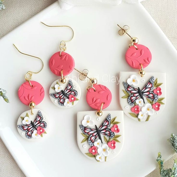 three pairs of pink and white earrings with flowers on them sitting on top of a plate