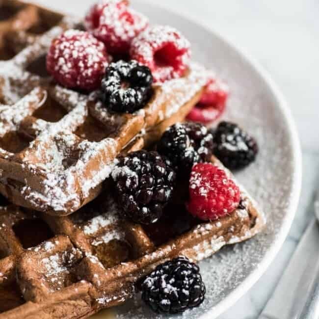 a white plate topped with waffles covered in powdered sugar and berries