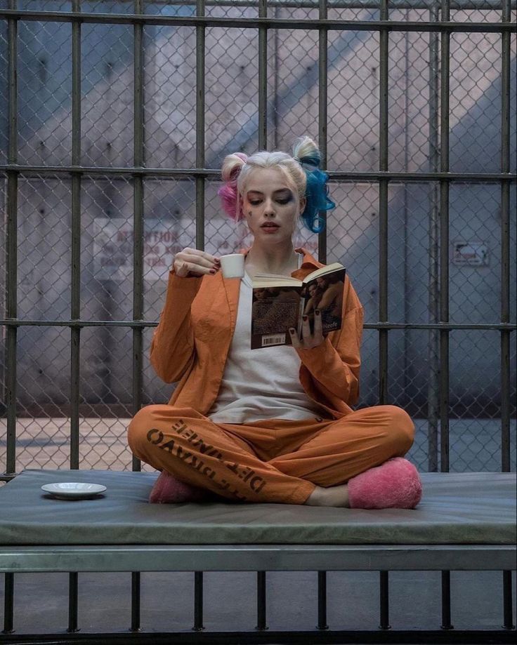 a woman sitting on top of a bench reading a book in front of a jail cell