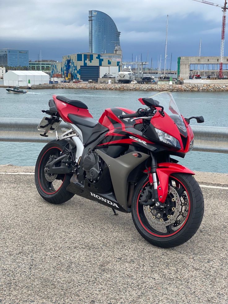 a red and black motorcycle parked next to the water