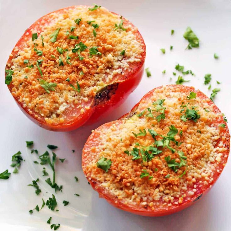 two stuffed tomatoes on a white plate with parmesan cheese and green garnish