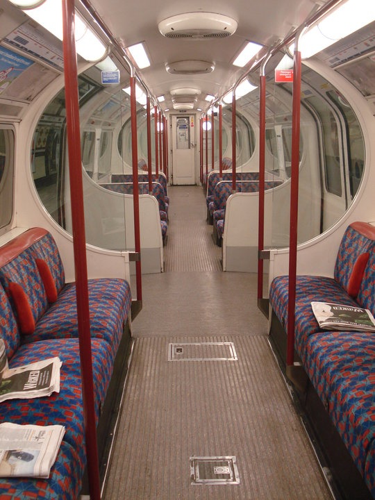 the inside of a train car with blue and red seats on each side, reading newspapers