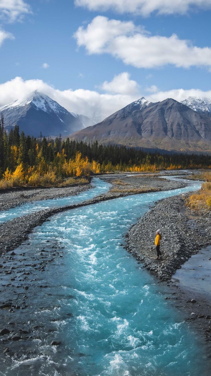 a man standing in the middle of a river with mountains in the backgroud