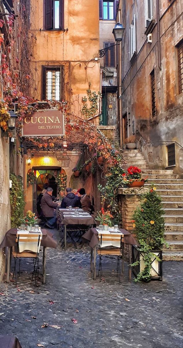 two people sitting at an outdoor table in the middle of a cobblestone street