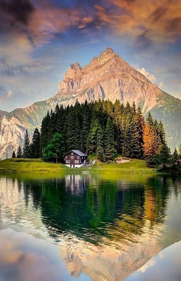 a lake surrounded by trees and mountains with a house on the shore in the foreground