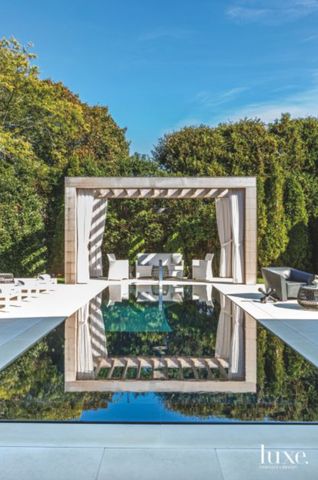 an outdoor swimming pool surrounded by trees and bushes with a pergolated gazebo in the middle