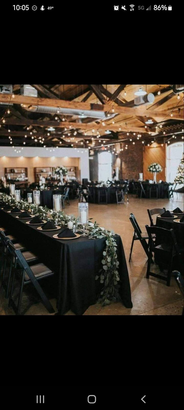 an indoor event with tables and chairs covered in black linens, greenery and candles