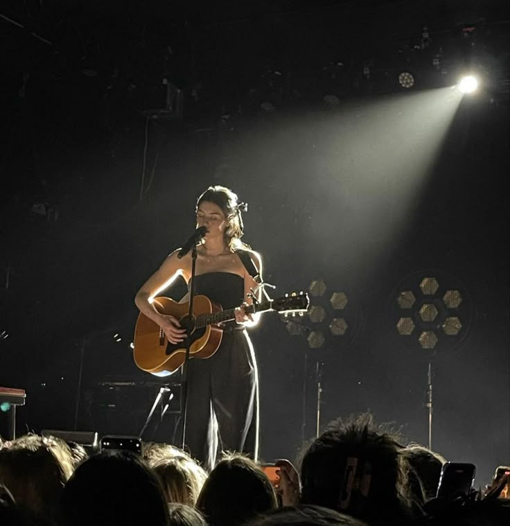 a woman standing on top of a stage holding a guitar in front of a crowd