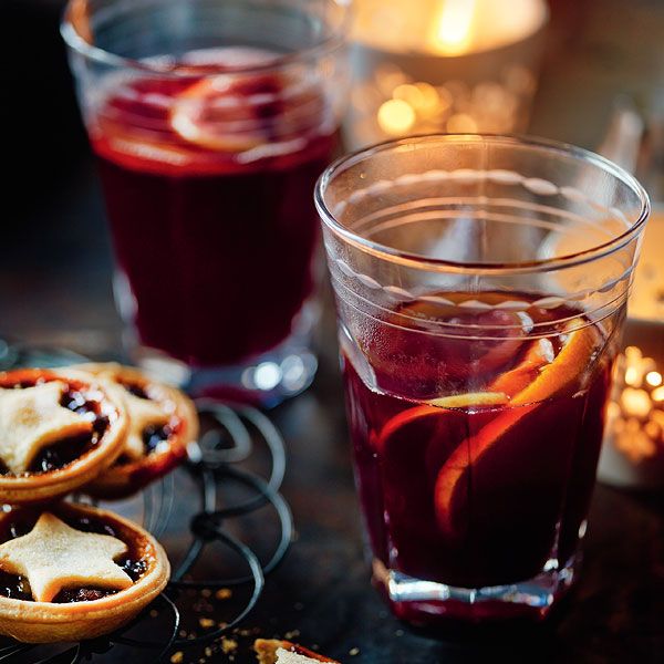 two glasses filled with red wine and orange slices next to some cookies on a table