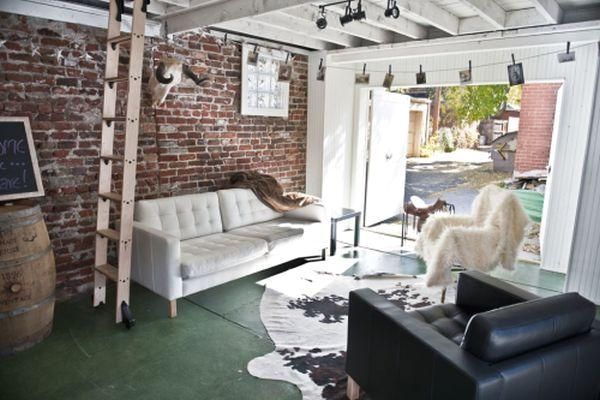 a living room filled with furniture next to a brick wall and wooden ladders hanging from the ceiling