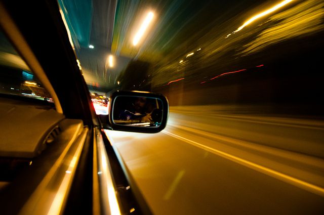 a car driving down a street at night with its lights on and the rear view mirror showing