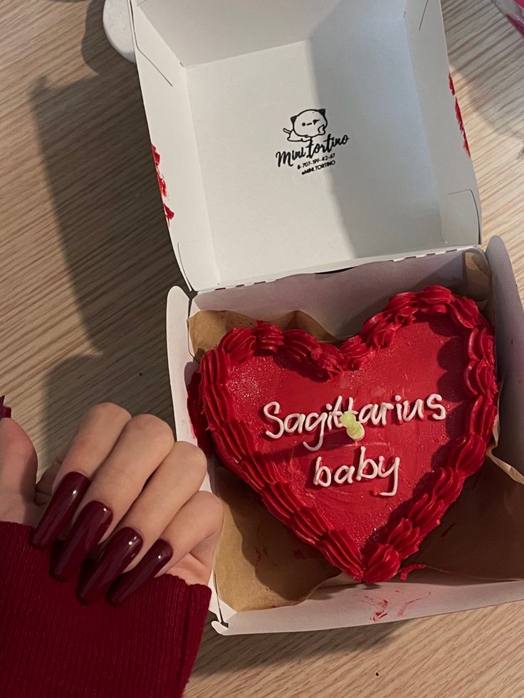 a heart shaped cake in a box with someone's hand next to it on a table