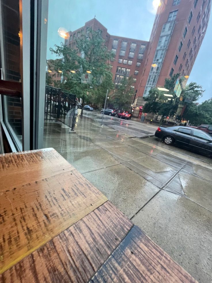 a wooden table sitting in front of a window next to a car parked on the street