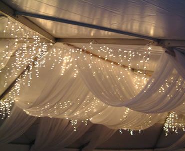 the inside of a tent with white drapes and lights