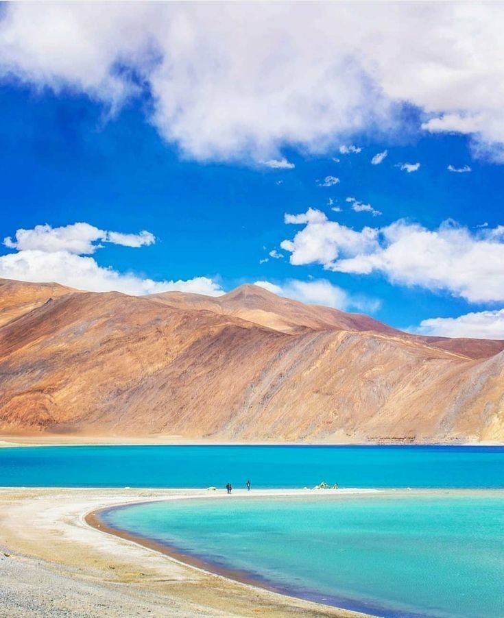 two people are standing on the shore of a large body of water with mountains in the background