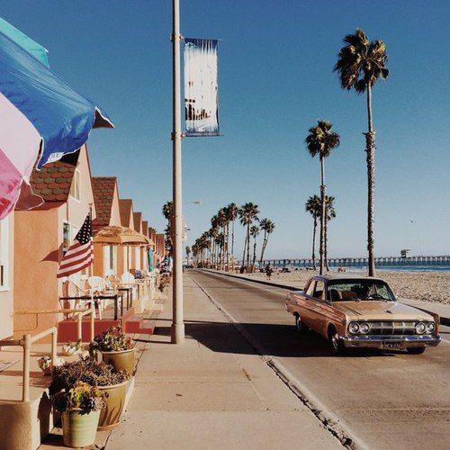 an old car is parked on the side of the road next to some palm trees