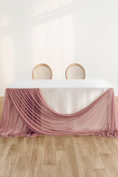 an empty table with two chairs and a pink cloth draped over it on a wooden floor