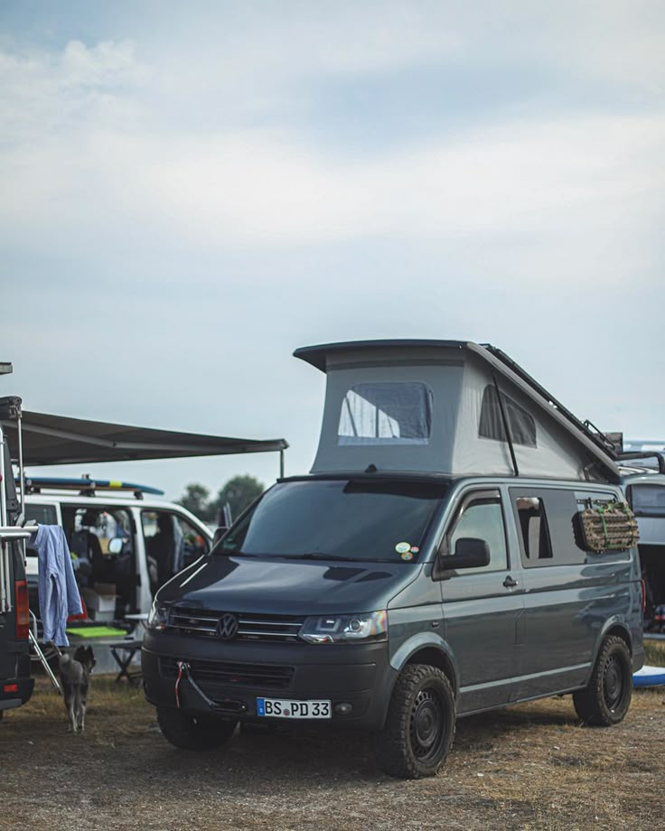 a van parked next to a camper trailer with people in the back ground looking at it