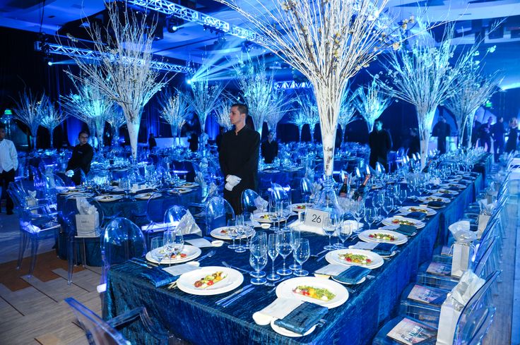 a table set up with plates and silverware in front of blue lit tablescapes