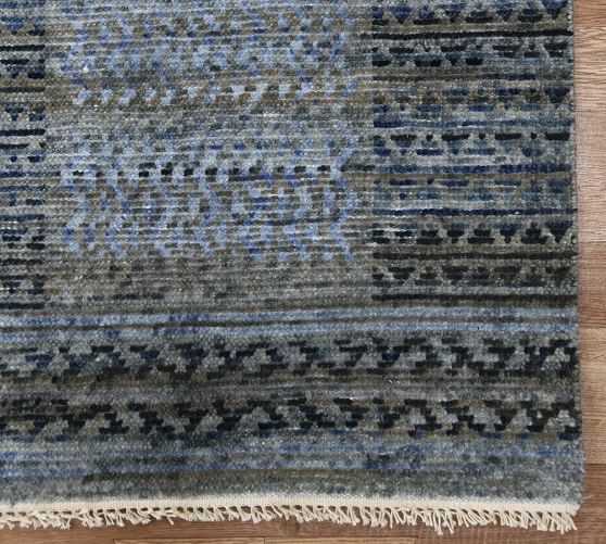 a blue and gray area rug with fringes on the bottom, in front of a wooden floor