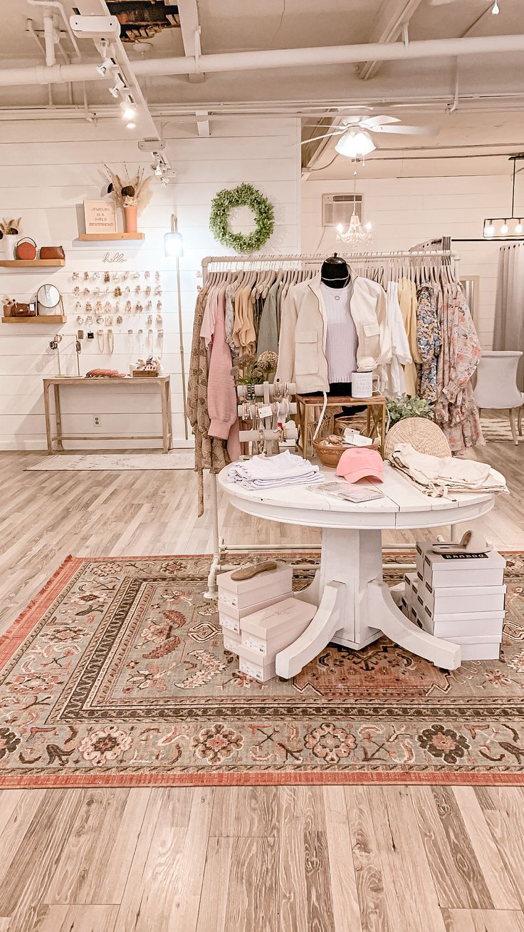 the inside of a clothing store with wooden floors and white tables, clothes on display