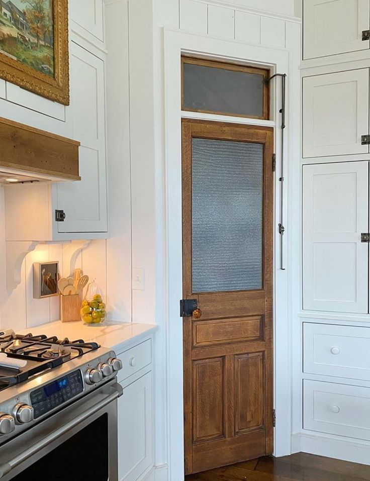 a kitchen with white cabinets and a wooden door in the center, next to a stove top oven