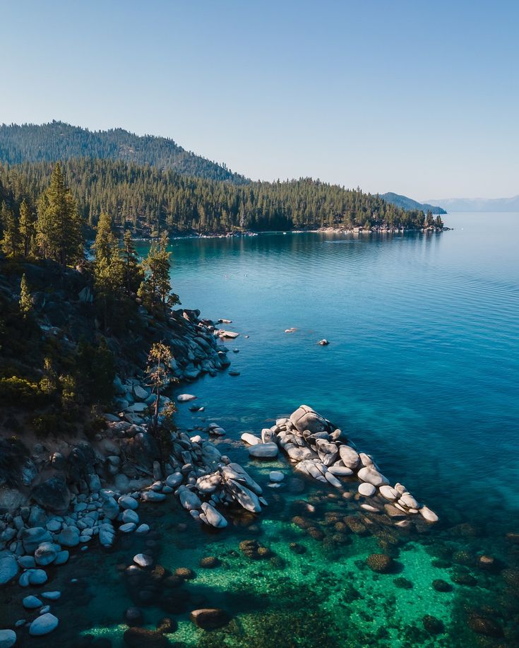 the water is crystal blue and clear with rocks in it, surrounded by pine trees