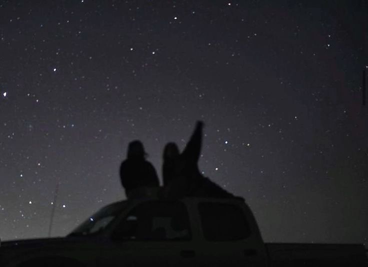 two people are sitting on the roof of a truck at night with stars in the sky