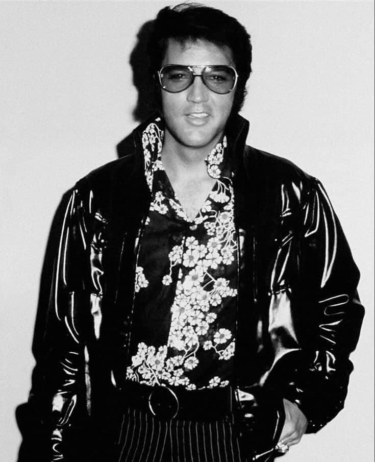 a man wearing sunglasses and a jacket standing in front of a wall