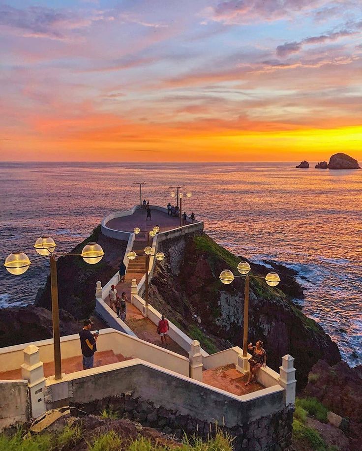 people are standing on the edge of a cliff overlooking the ocean