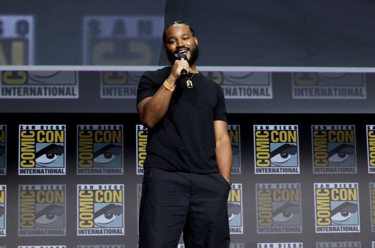 a man standing in front of a microphone on top of a stage with comic panels behind him