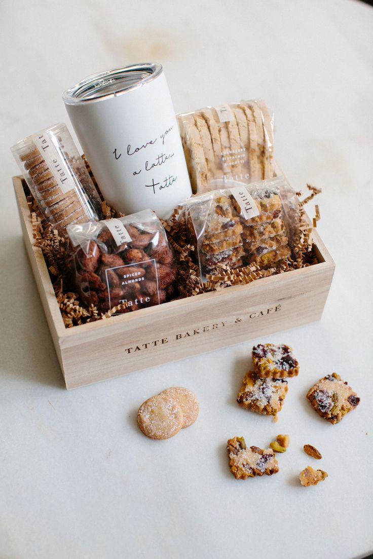 a wooden box filled with cookies and crackers next to a coffee mug on a table