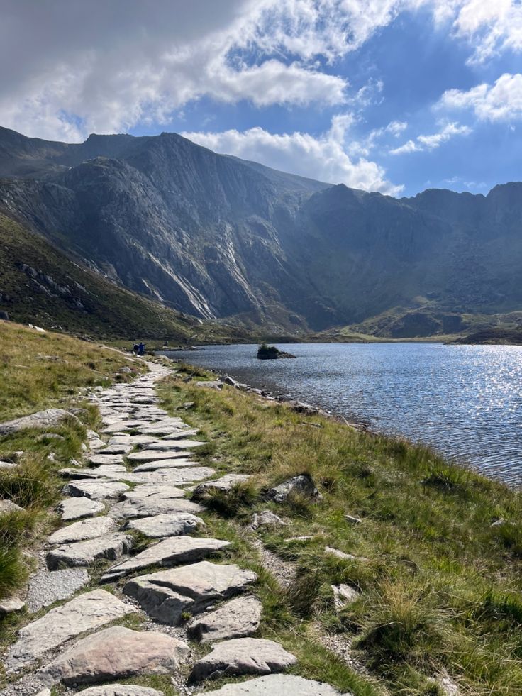 a stone path leading to a lake with mountains in the background