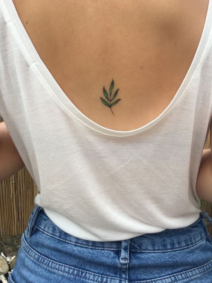 the back of a woman's neck with a small green leaf tattoo on it