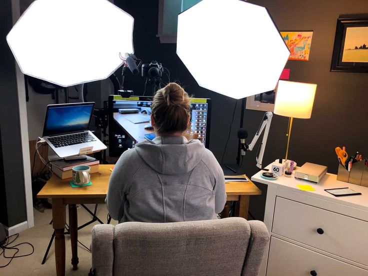 a woman sitting in front of a laptop computer on top of a wooden desk next to two white hexagonal lights