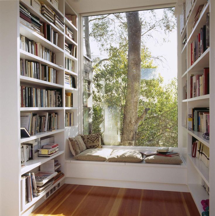 there is a window seat in front of the bookshelves