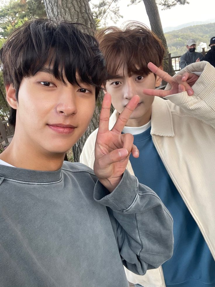 two young men standing next to each other with their fingers up in the air and making peace signs