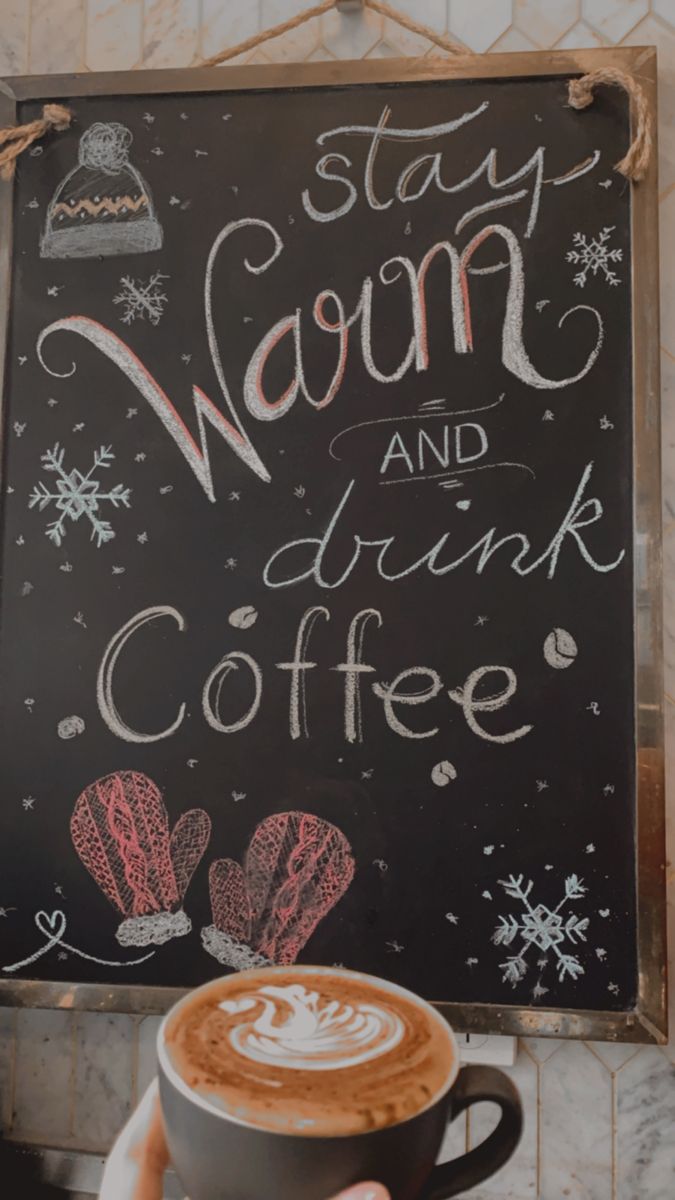 a person holding a cup of coffee in front of a chalkboard sign that says stay warm and drink coffee