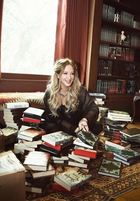 a woman is sitting on the floor surrounded by many books in front of a window