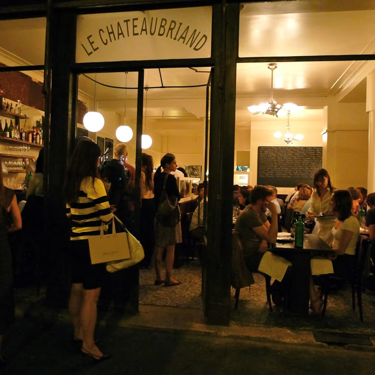 a group of people sitting at tables in front of a restaurant with the door open