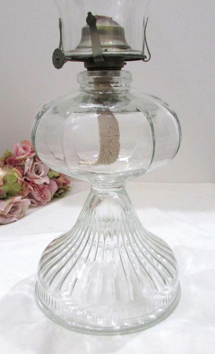 an old fashioned glass oil lamp on a white tablecloth with flowers in the background