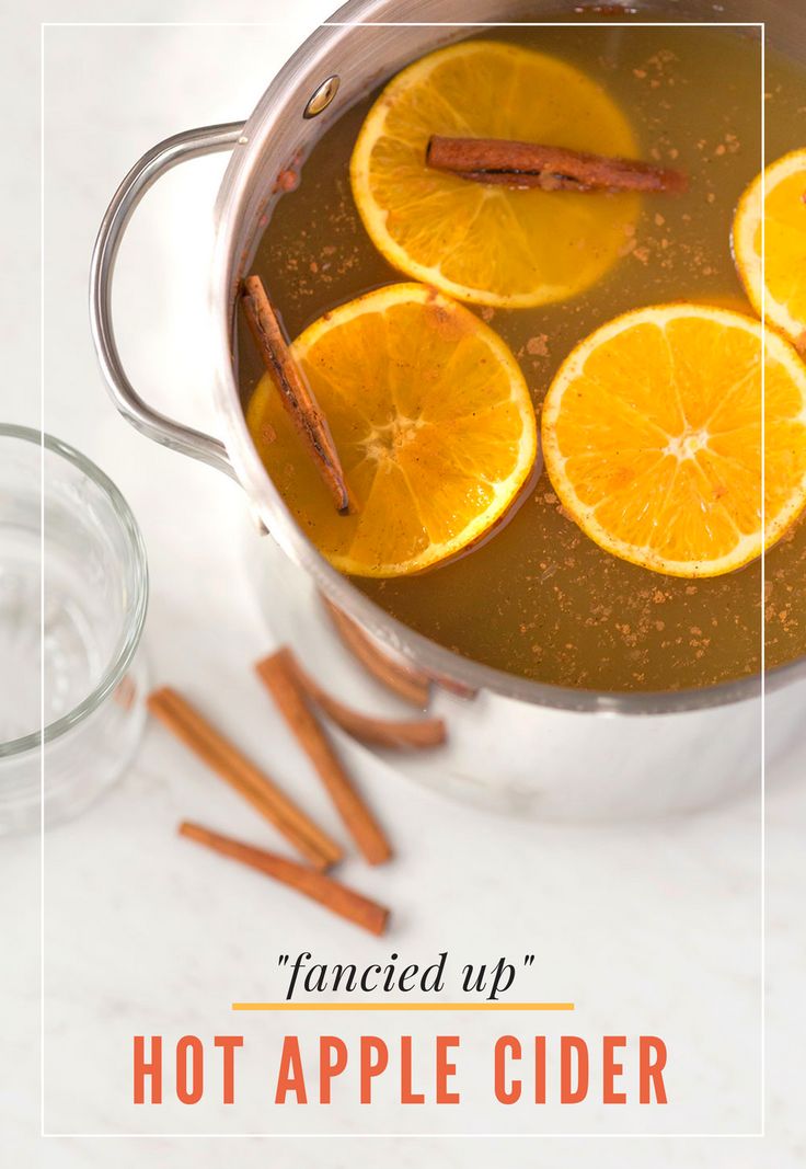 hot apple cider with cinnamon sticks and orange slices in the pot, surrounded by spices