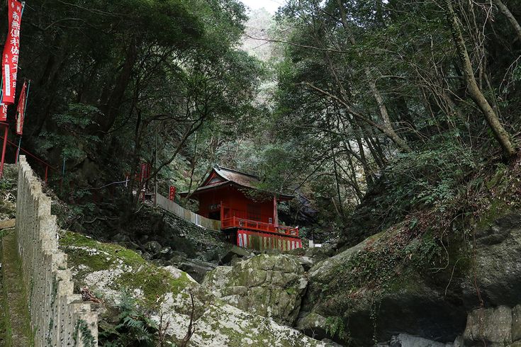 a small red building in the middle of a forest with trees and rocks around it