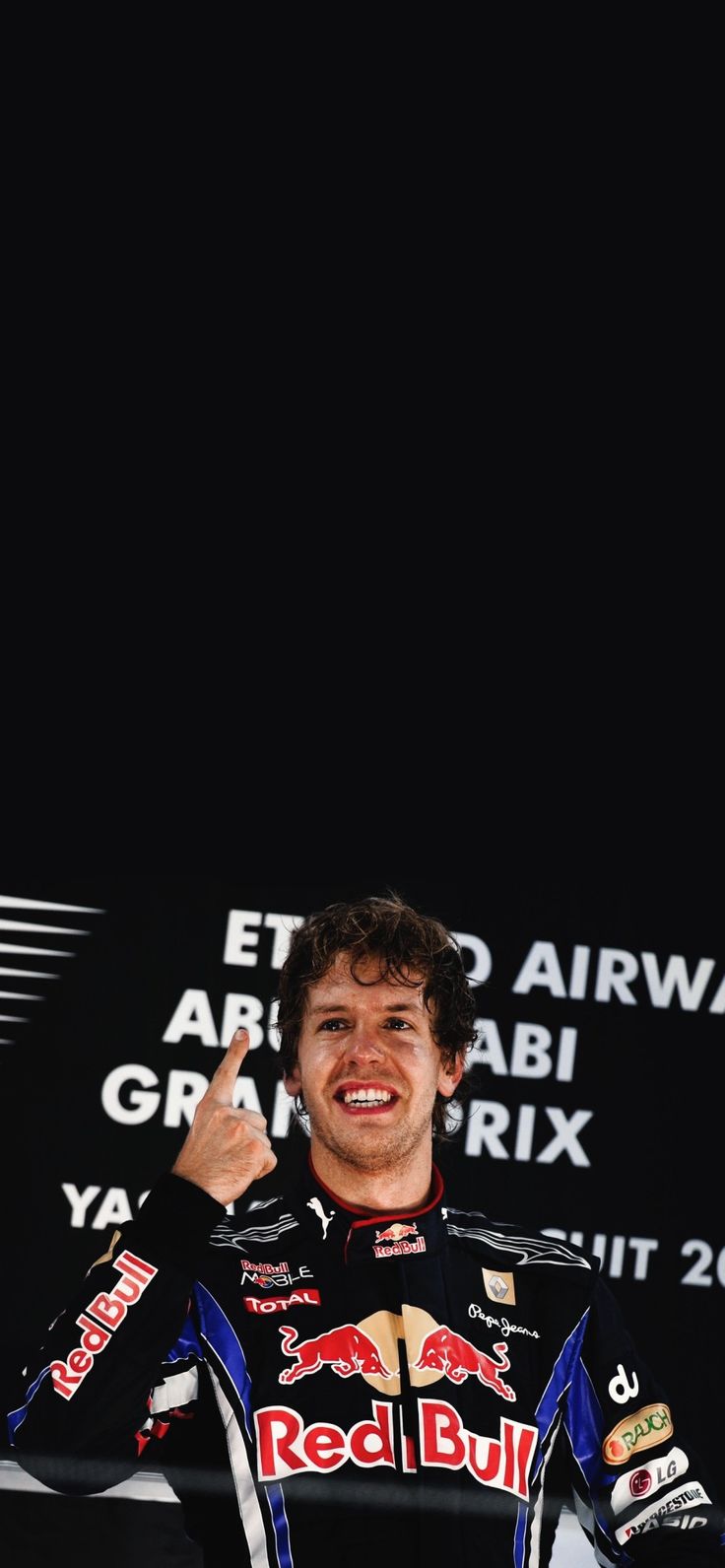 a man giving the thumbs up while standing in front of a black wall with red bull written on it