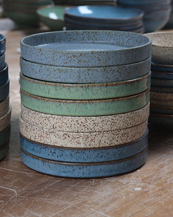 a stack of blue and green bowls sitting on top of a wooden table next to stacks of plates