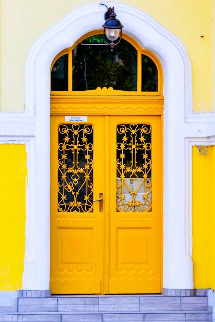 a yellow door with wrought iron work on the front and side doors are open to let in light