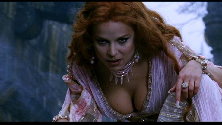 a woman with red hair and jewelry on her chest is posing for the camera while wearing an elaborate dress