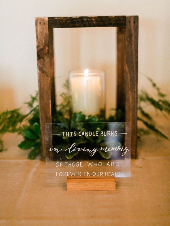 a wooden frame with a candle and some plants in it on top of a table